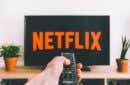 person holding a remote control pointed at a TV displaying the Netflix logo